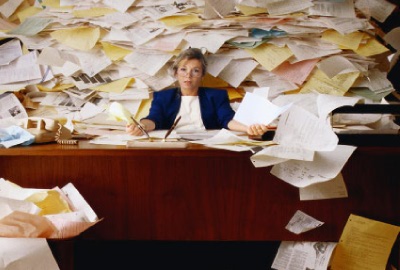 Image of woman at a desk in front of mountain of papers depicting the need to be ready for risky projects.