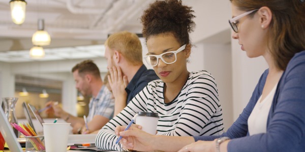 Image of a man and a woman sitting across from each other at a table, both are in front of notebook computers, depicting them providing constructive criticism of the other's work.