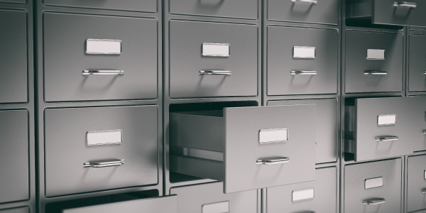 Image of person sitting behind a towering stack of papers punctuating the need for project document management.