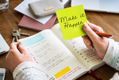 Person working on to-do list with note 'make it happen' signifying the need to motivate project teams.